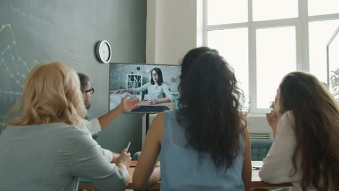 一群商务人士进行视频通话，与女同事聊天，看着坐在工作场所办公桌上的显示器