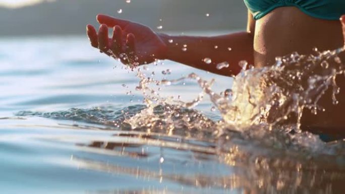 特写: 女性游客在日落时在海洋中冷却时泼水