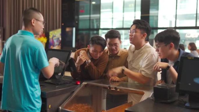 前酒吧柜台的亚洲华裔年轻人在电影院放映电影前订购了无接触付款的爆米花