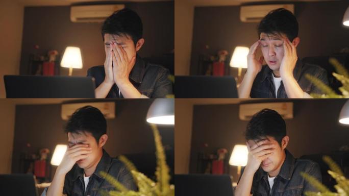 在家庭办公室工作到很晚时，使用笔记本电脑的亚洲男子感到困倦，眼睛上有压力或沮丧