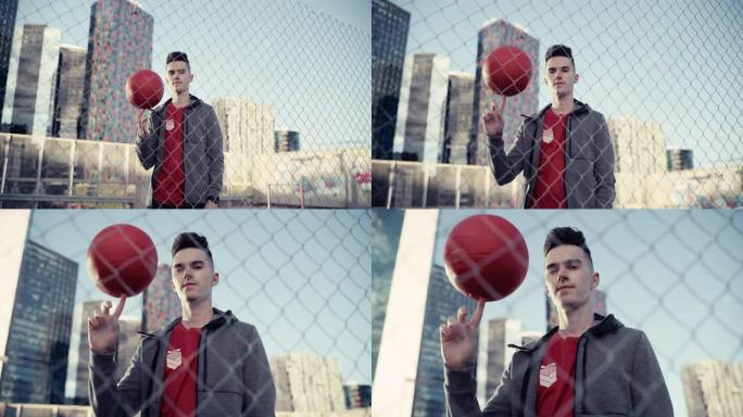 特写一位时尚的年轻足球运动员摆姿势拍照，手指上旋转一个红球的肖像。英俊的足球运动员站在城市的篱笆后面