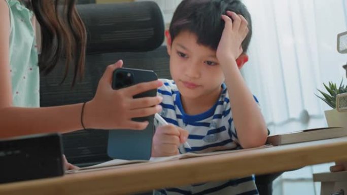 特写的亚洲姐姐正在通过在家中智能手机上展示来教弟弟做作业。