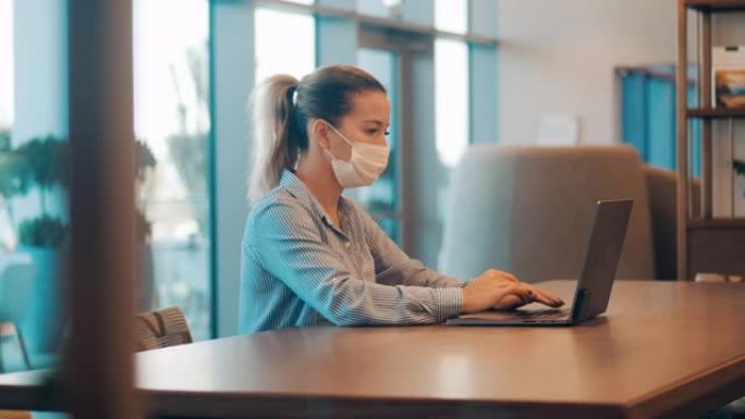 一个戴着口罩的女人正在桌上的笔记本电脑上工作