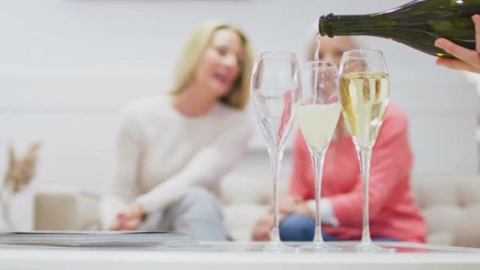 普罗塞克或香槟被倒入玻璃杯中的特写镜头，两名妇女坐在沙发上，背景是慢动作拍摄