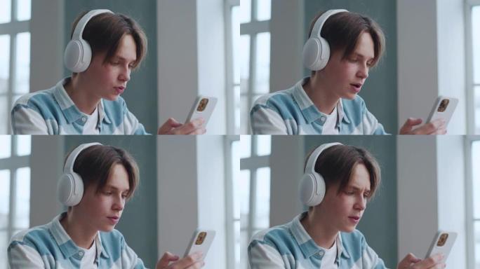 戴着耳机的少年在家里听音乐。迷人聪明的年轻人放松在音频电话上的歌曲声音。英俊的青少年男学生在最喜欢的