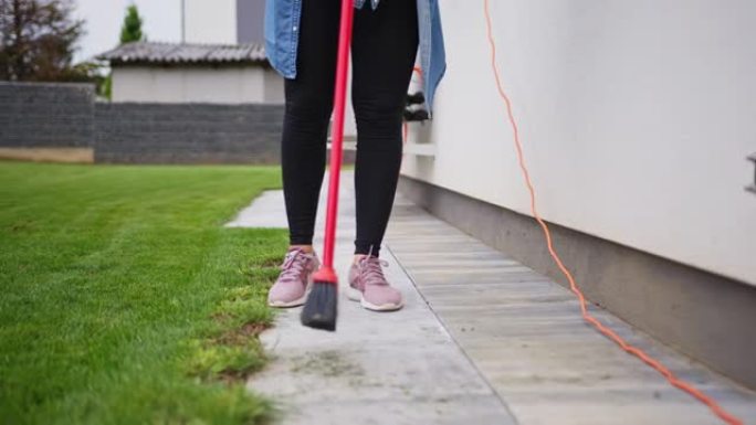 女人用大扫帚清理房子的后院