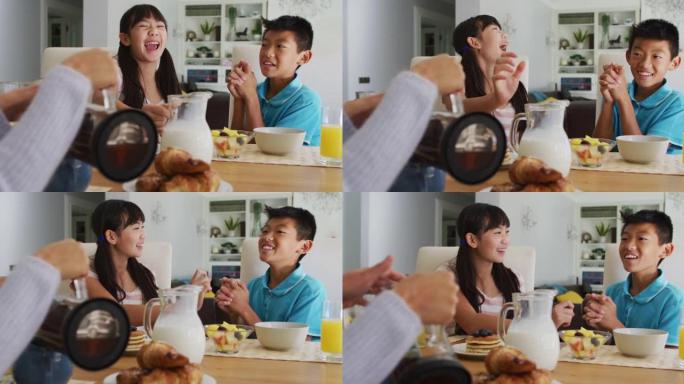 快乐的亚洲兄妹在厨房吃早餐，和父母一起笑