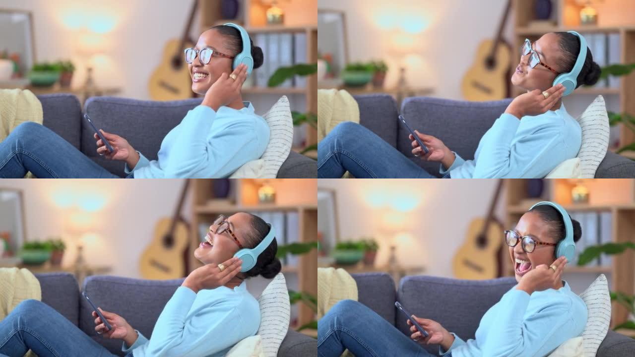女人戴着耳机在手机上播放音乐，在家放松时唱歌。周末，快乐的非洲女性在沙发上听她最喜欢的歌曲