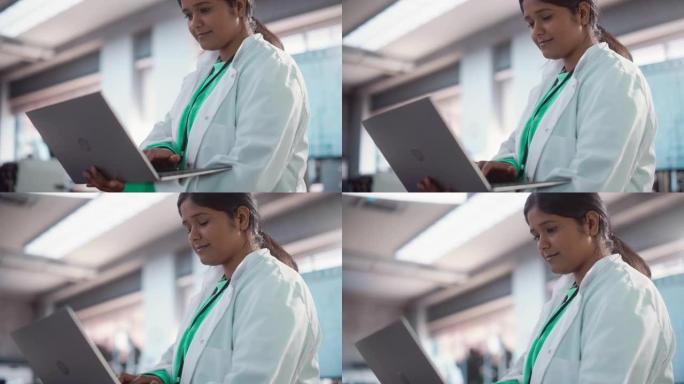 年轻的印度女专家穿着实验室外套微笑着使用笔记本电脑的肖像特写。专业而成功的女性担任工程师，开发高科技