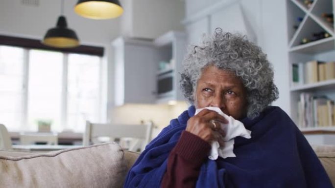 生病的非裔美国高级妇女坐在家里的沙发上，上面盖着毯子