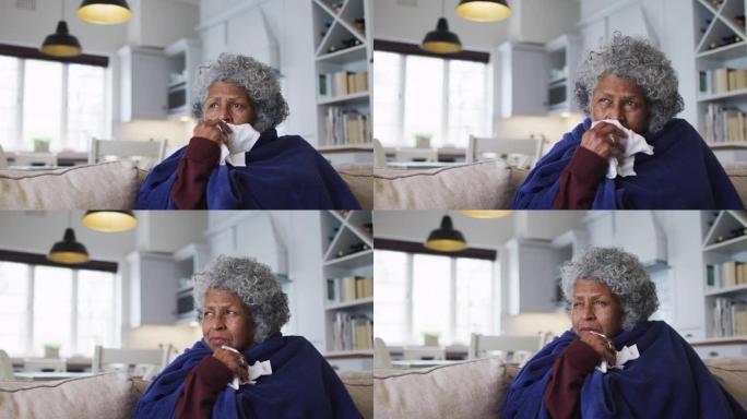 生病的非裔美国高级妇女坐在家里的沙发上，上面盖着毯子