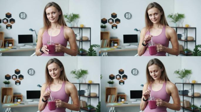 可爱的女运动员拿着冰沙微笑站在家里的慢动作肖像