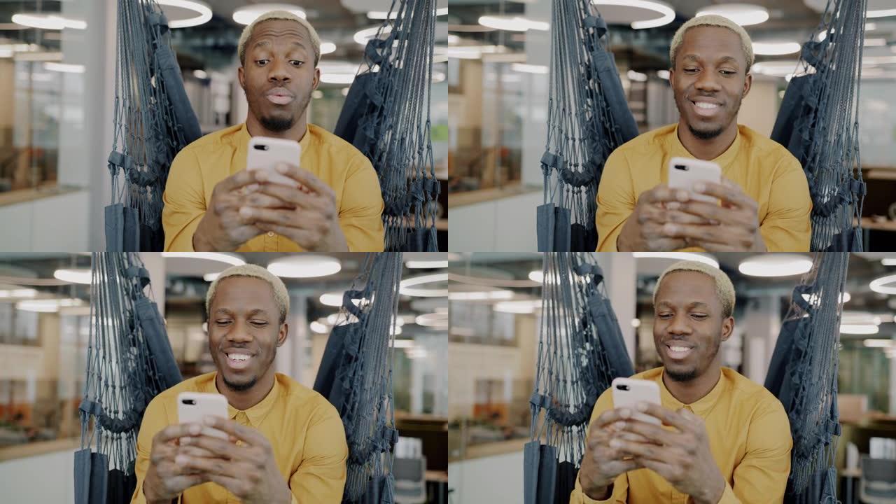 快乐的非洲裔美国员工使用智能手机微笑坐在现代办公室的吊椅上