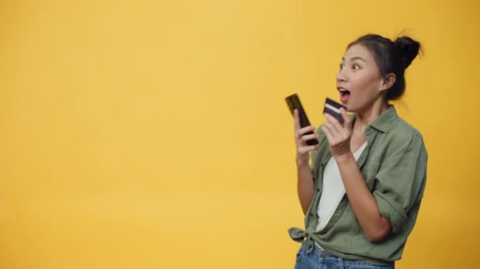 美丽迷人的亚洲青年孤立女士享受手机滚动电子商店和信用卡购买网上商店，成功支付黄色背景。