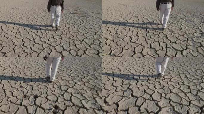 气候变化。由于气候变化和全球变暖造成的干旱，一个饱受摧残的农民走过干旱大坝的有图案的开裂的泥面