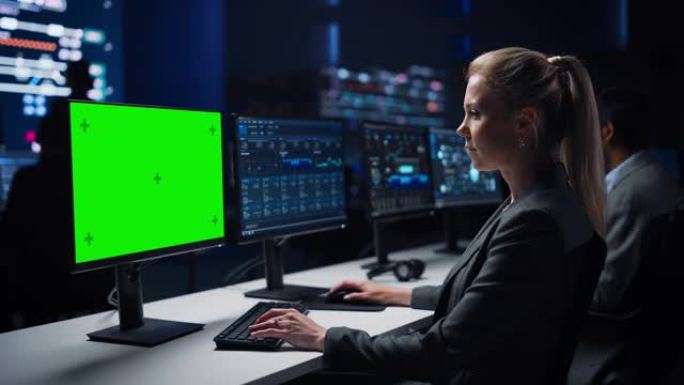 自信的女性数据科学家在大型基础设施控制室的绿色色度键屏幕计算机上工作。专家使用显示图表、信息的计算机