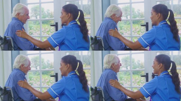 穿着制服的女护理人员与坐在养老院休息室的轮椅上的老人交谈