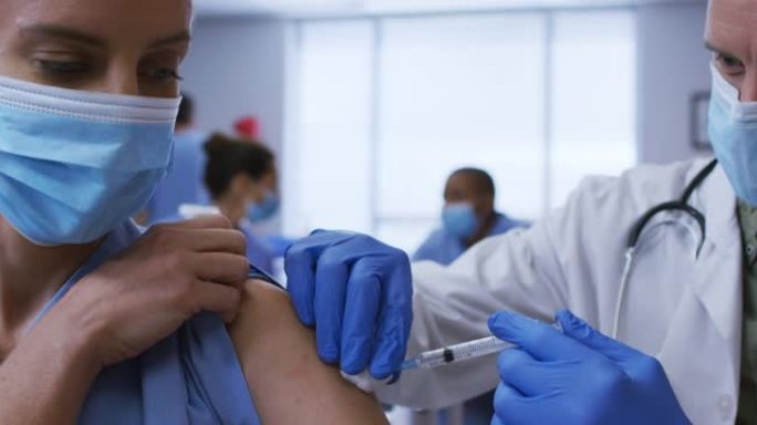 高加索男医生在医院给女同事接种covid疫苗，都戴着口罩