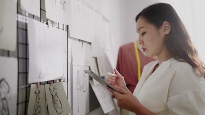 时装设计师用墙上的素描纸在她的数字平板电脑上素描服装