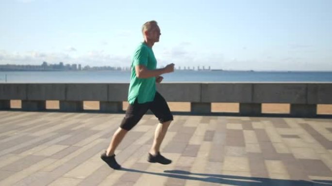 穿着绿松石t恤的奔跑男子的侧视图，背景是大海和天空