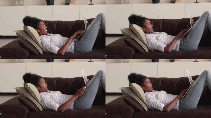 非洲妇女躺在沙发上，配有便携式无线电脑