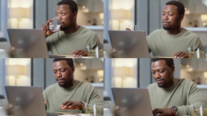年轻的非洲裔美国商人一边喝水一边在家工作，一边在桌子上用笔记本电脑工作。男性自由职业者看起来很累，喝