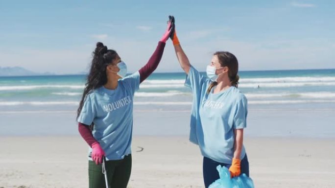 两名穿着志愿者t恤和口罩的不同女性从海滩捡垃圾