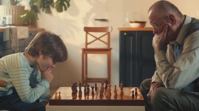侧视小男孩思考，在家对老爷爷下棋。情报概念。