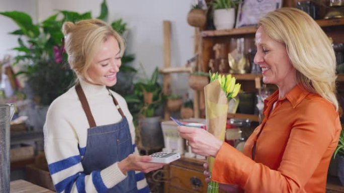 成熟的女人在花店购买一束使用非接触式卡支付的郁金香-慢动作拍摄