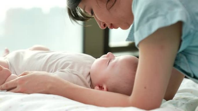一位年轻的母亲深情地亲吻躺在床上的婴儿，传达出母亲对婴儿的爱。