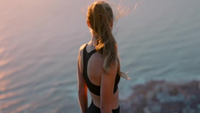 山顶上健康的女人在日落时看着海景站在悬崖边享受自由的女孩在考虑登顶之旅