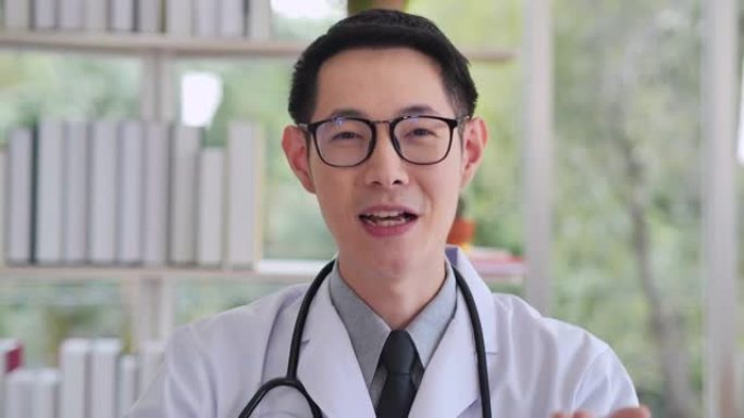 向32岁的中国男性医生肖像，在医疗诊所的远程地点或在家工作时，在视频会议上看摄像机。远程保健概念。
