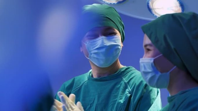 亚洲团队合作四名专业外科医生和助手鼓掌和微笑完成手术。医生团队庆祝成功拯救了手术室的生命患者。商业庆