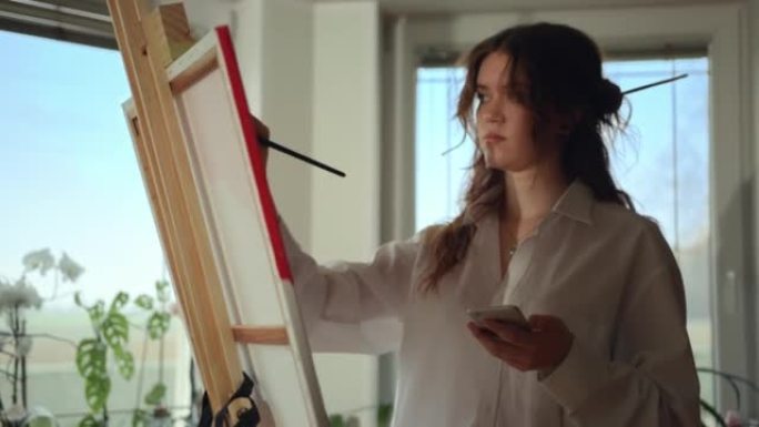 SLO MO Young女艺术家在画布上绘画时使用手机