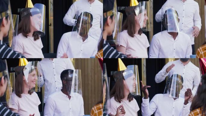 快乐的年轻白人妇女和戴着新型冠状病毒肺炎塑料面罩的多民族朋友庆祝生日跳舞。