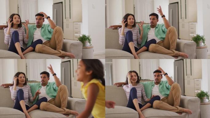 愤怒的西班牙裔父母坐在沙发上争论着跳舞的女儿