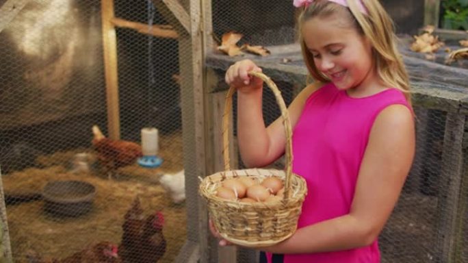 快乐的高加索女孩拿着一篮子鸡蛋站在花园里的鸡舍旁