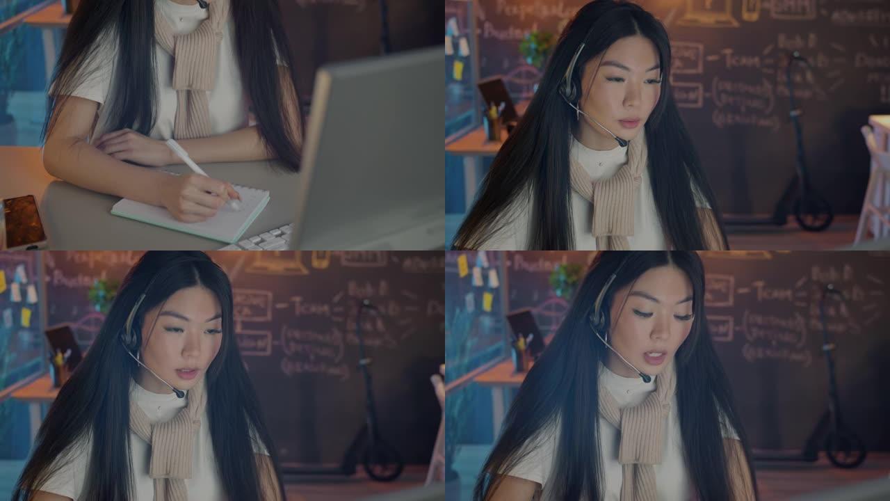 亚洲女孩客户支持工作者在黑暗的办公室里用耳机说话和做笔记