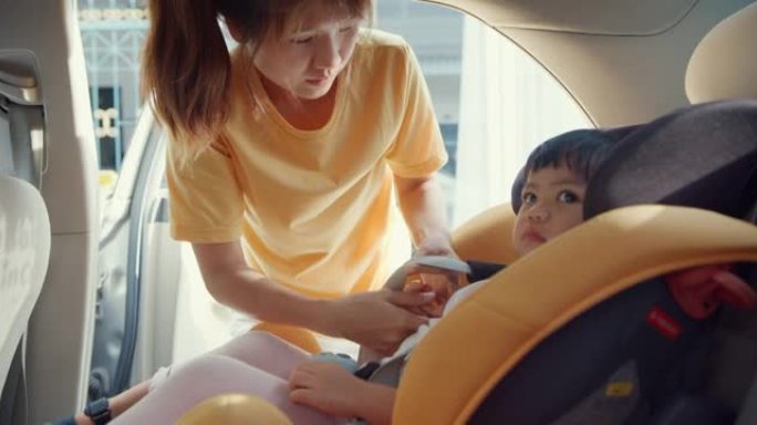 快乐快乐的亚洲家庭妈妈在和蹒跚学步的女孩准备乘车旅行之前，系好儿童汽车座椅的安全带。