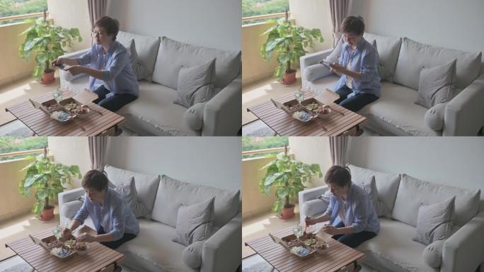 亚洲中国妇女在客厅用智能手机拍照外卖食物马来西亚食物nasi kerabu