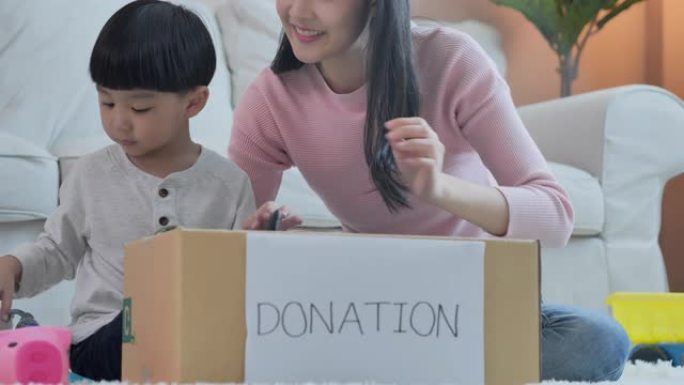 快乐的亚洲母亲教小男孩关于可持续性的儿子如何在家里将玩具包装到捐赠盒中，教/学习捐赠概念。