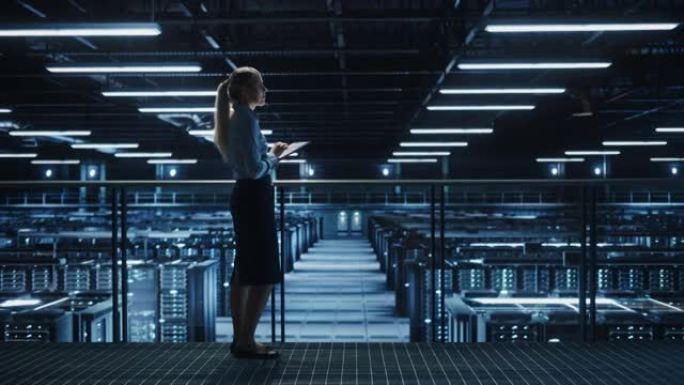 女性IT专家在数据中心使用平板电脑，走在俯瞰大服务器场云计算设施的桥上。女商人，电子商务企业家。基座