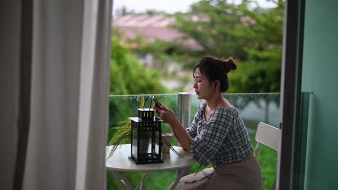 亚洲华人妇女享受她的闲暇时间在阳台用她的手机听歌曲上网冲浪