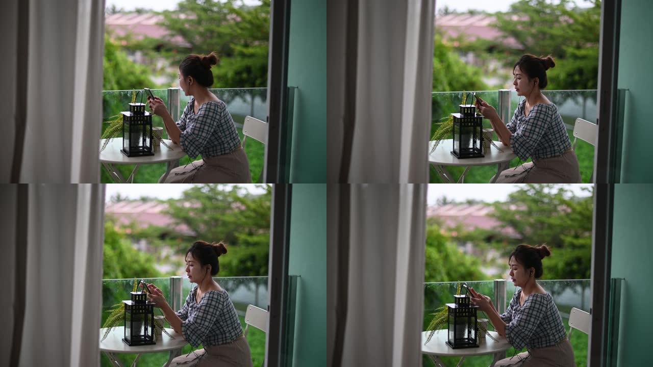 亚洲华人妇女享受她的闲暇时间在阳台用她的手机听歌曲上网冲浪