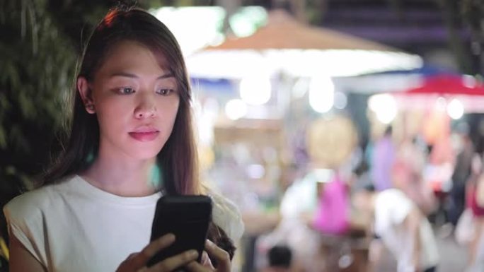 年轻的亚洲女性在步行街或街头食品市场旅行和使用智能手机