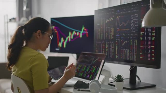 亚洲女性在家中在线交易股票时在计算机显示器上分析图表