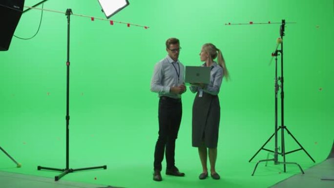 男女同事穿着便服聊天，在绿屏上使用笔记本电脑模拟色键工作室。商业，企业办公室，工作，技术概念。