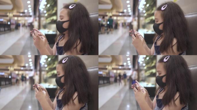 女孩与保护面罩，以防止冠状病毒或新型冠状病毒肺炎使用智能手机在购物中心