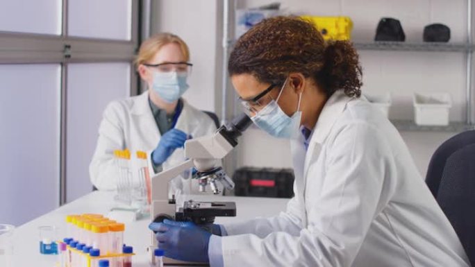 穿着个人防护装备的实验室女工作人员在实验室用显微镜分析血样