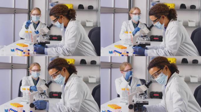 穿着个人防护装备的实验室女工作人员在实验室用显微镜分析血样